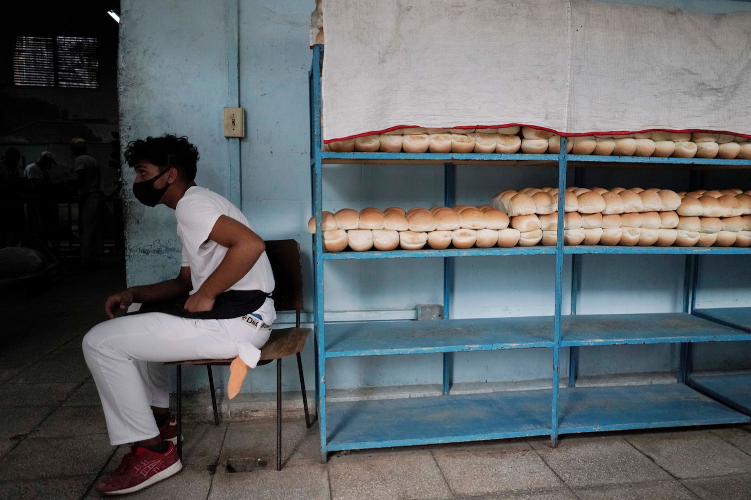An employee sits beside bread stored on shelves inside a bakery in Havana, Cuba, May 18, 2021. (Reuters)