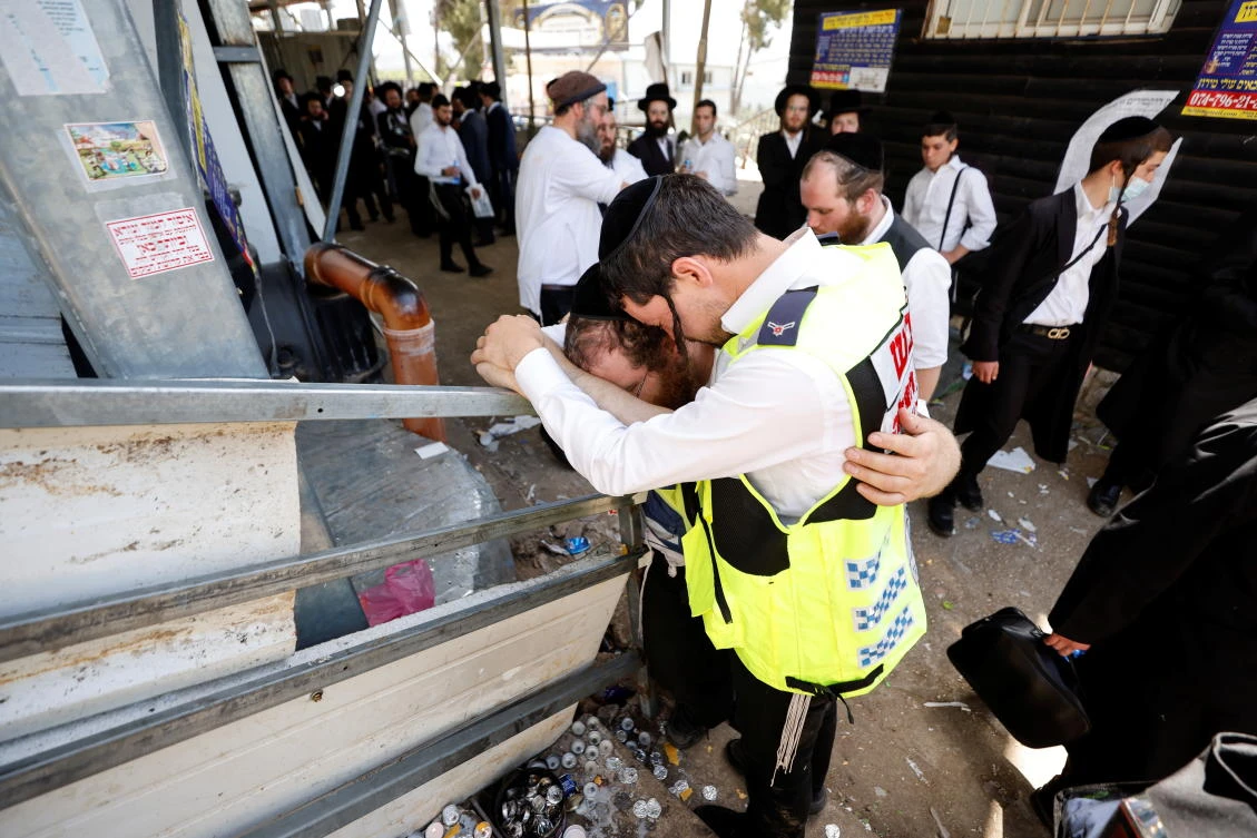 Emergency workers hug as they react at the site where dozens were crushed to death in a stampede at a religious festival, as the country observes a day of mourning, at Mount Meron, Israel. (Reuters)