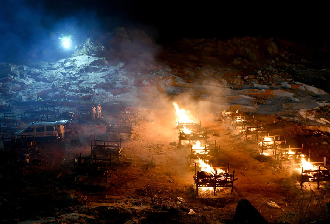 Volunteers stand next to burning pyres of persons who died due to the coronavirus disease (COVID-19), at a crematorium on the outskirts of Bengaluru. (Reuters)