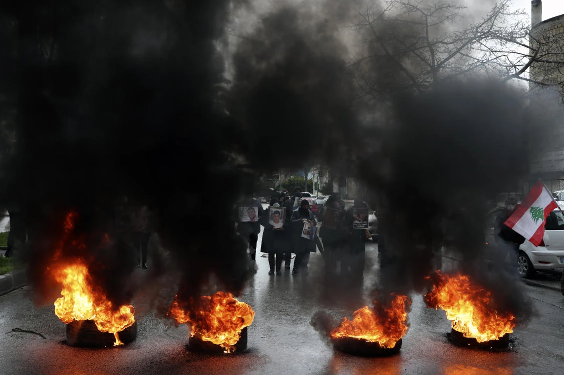 Relatives of victims killed in the Aug. 4, 2020 Beirut port explosion holding their portraits as they burn tires to block a road during a sit-in outside Lebanon’s Justice Palace Lebanon. (AP)