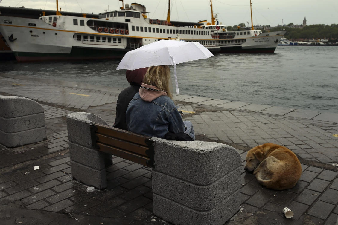 People sit under rain by the nearly-deserted Golden Horn market amid strict lockdown in Turkey that on Saturday saw daily COVID-19 cases fall below 20,000 for first time since March 17. (AP)