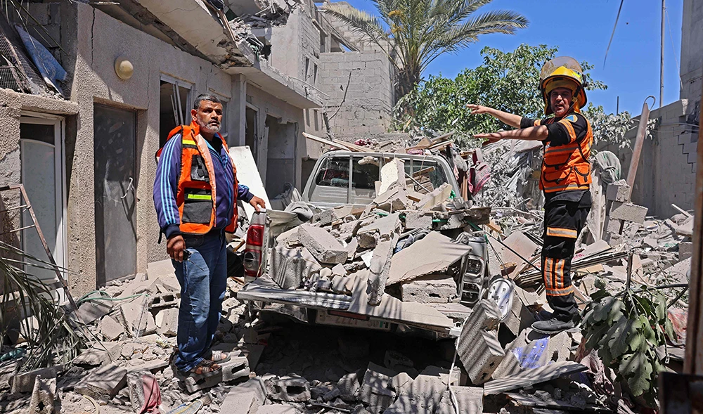 Palestinian rescue teams inspect the damage outside a destroyed residential building targeted by Israeli airstrikes on May 18, 2021 in Rafah, in the southern Gaza Strip, near the border with Egypt. (AFP)