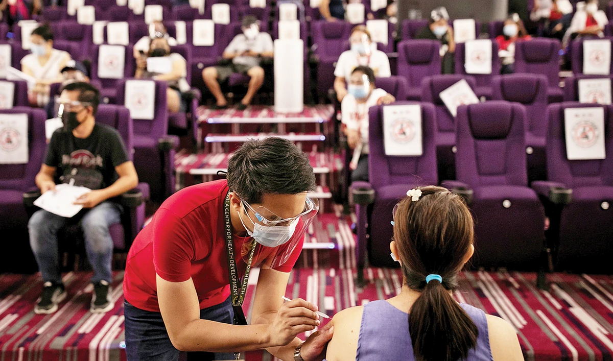 A health worker inoculates a woman with the AstraZeneca COVID-19 vaccine, inside a closed cinema in Taguig, Metro Manila, on Monday. (Reuters)