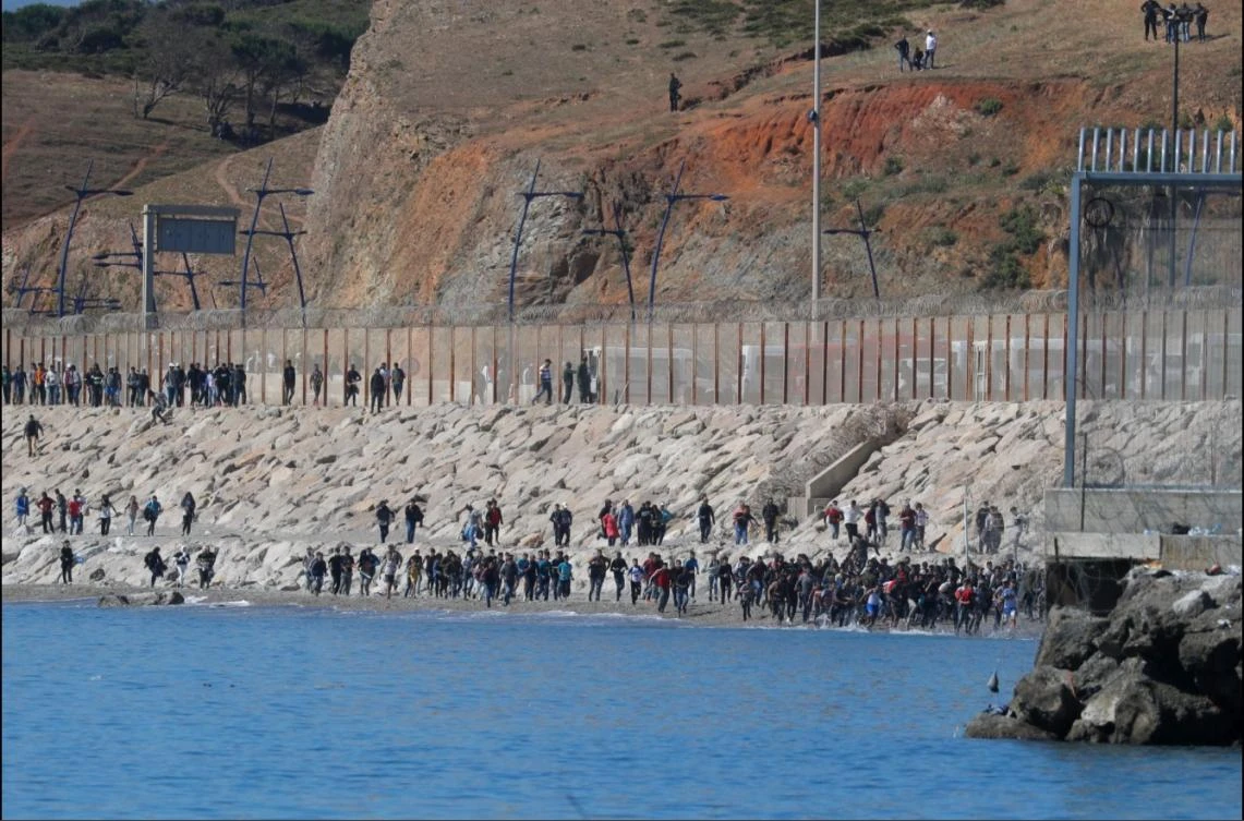 Migrants run toward the fence separating Morocco from Spain, after thousands swam across the border, in Ceuta, Spain, May 19, 2021. (Reuters)