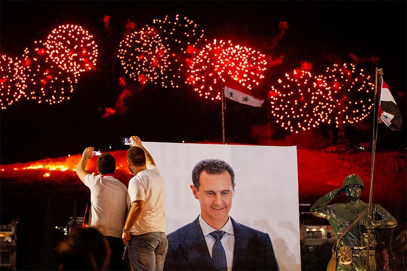 A poster depicting Syria’s president Bashar al- Assad is seen as supporters of him celebrate after the results of the presidential election announced that he won a fourth term in office, in Damascus, Syria, May 27, 2021. (REUTERS)