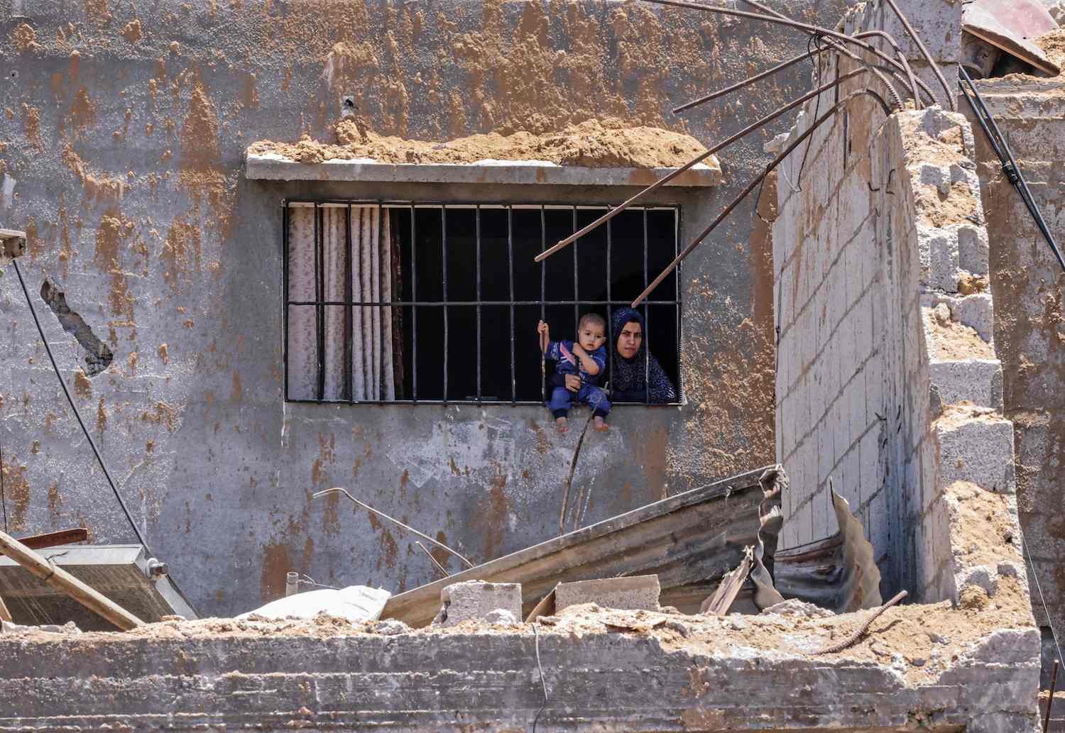 A Palestinian woman holds her child as they look out of the window in Khan Yunis in the southern Gaza Strip on May 26, 2021. (AFP)