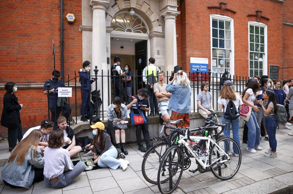 People play a card game while queueing outside a vaccination centre at the Hunter Street Health Centre in London. (File/Reuters)