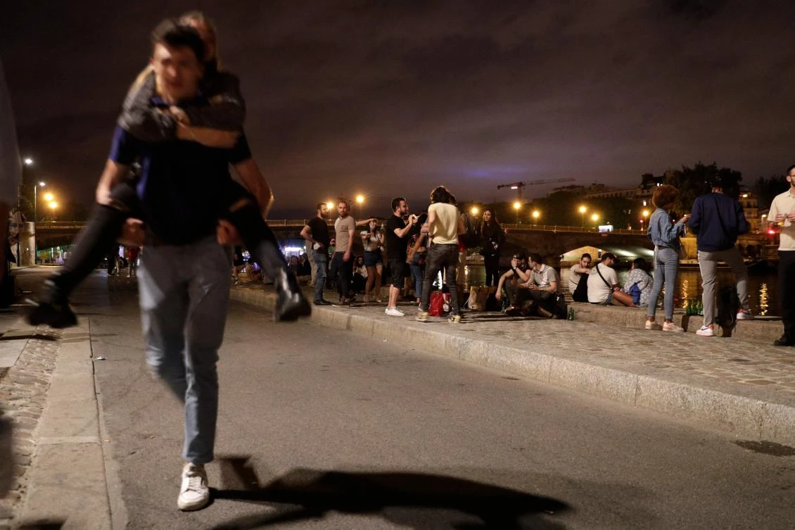 People stand on the banks of the Seine River past the 11 p.m. COVID-19 curfew early on June 12, 2021, after people gathered nearby at Les Invalides for an unauthorized outdoor party. (AFP)