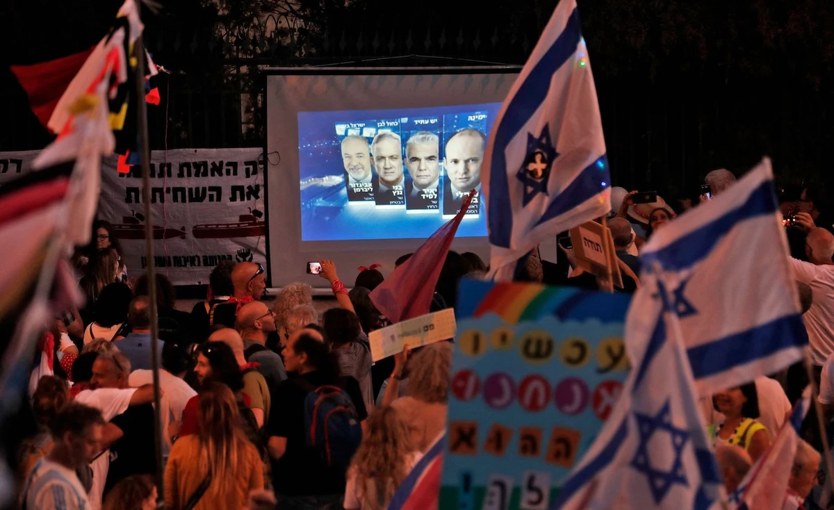 Israeli demonstrators gather near a screen showing a projection of the faces of the heads of a new coalition government. (AFP)