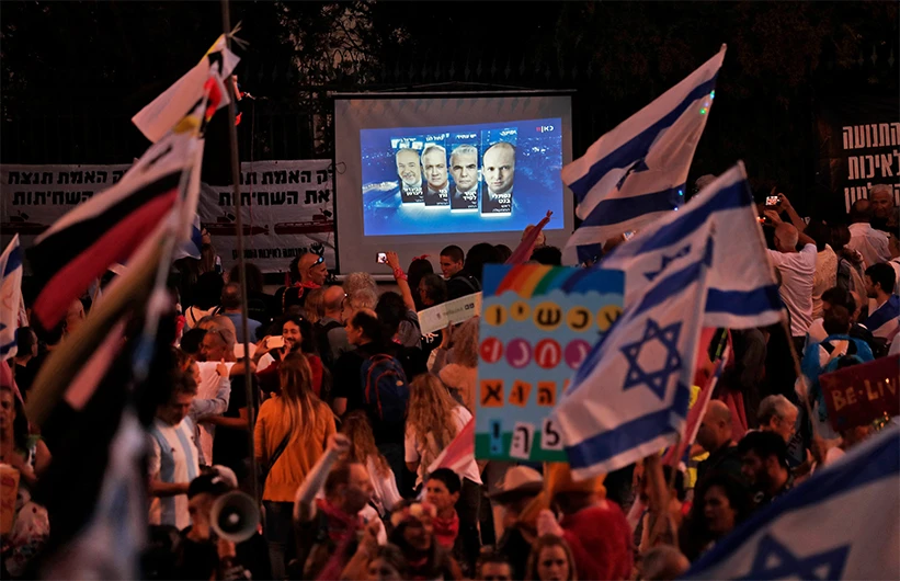 Israeli demonstrators gather near a screen showing a projection of the faces of the heads of a new coalition government, during a supportive rally in front of the Knesset during a parliamentary vote, in Jerusalem on June 13, 2021. (AFP)