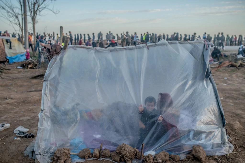 A Syrian woman sits in a tent with her son as others wait for food distribution on March 3, 2020 in front of the Pazarkule border crossing to Greece, in Edirne. (File/AFP)