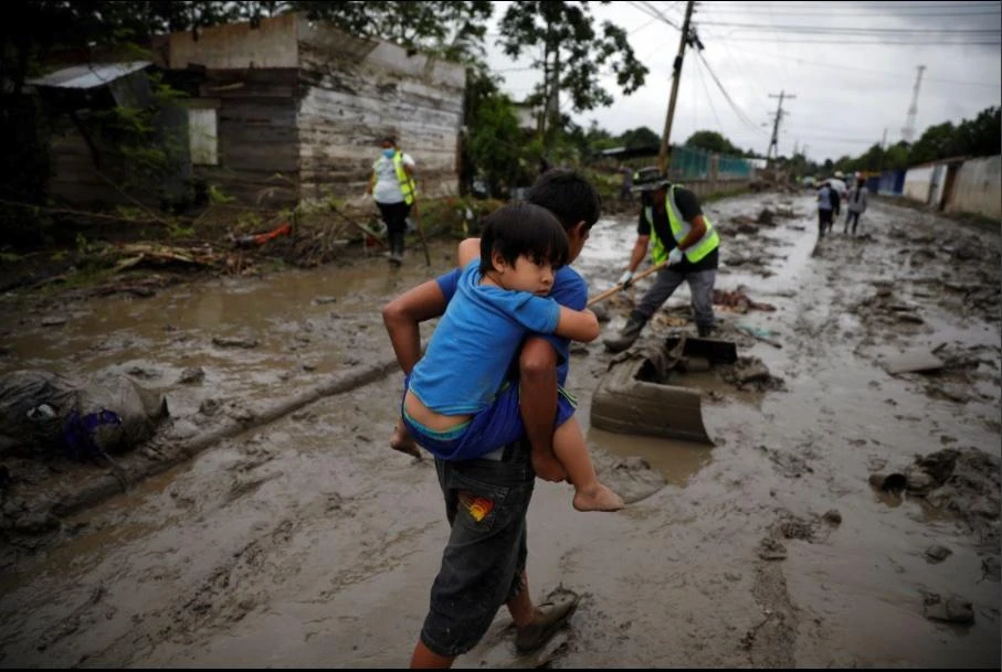 A child carries his brother in a street covered in mud after the floods caused by the rains brought by Hurricanes Eta and Iota, in La Lima, Honduras December 8, 2020. (Reuters)