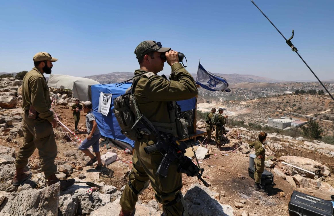 Israeli soldiers observe the Palestinian village of Beita with binoculars as settlers evacuate the newly-established wildcat outpost of Eviatar in Beita, near Nablus in the occupied West Bank. (File/AFP)