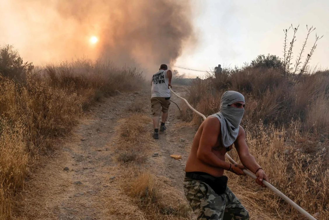 Volunteers help carry a firehose in an effort to contain a fire near the Kotsiatis area on the outskirts of Cyprus’ capital Nicosia on July 4, 2021. (AFP)