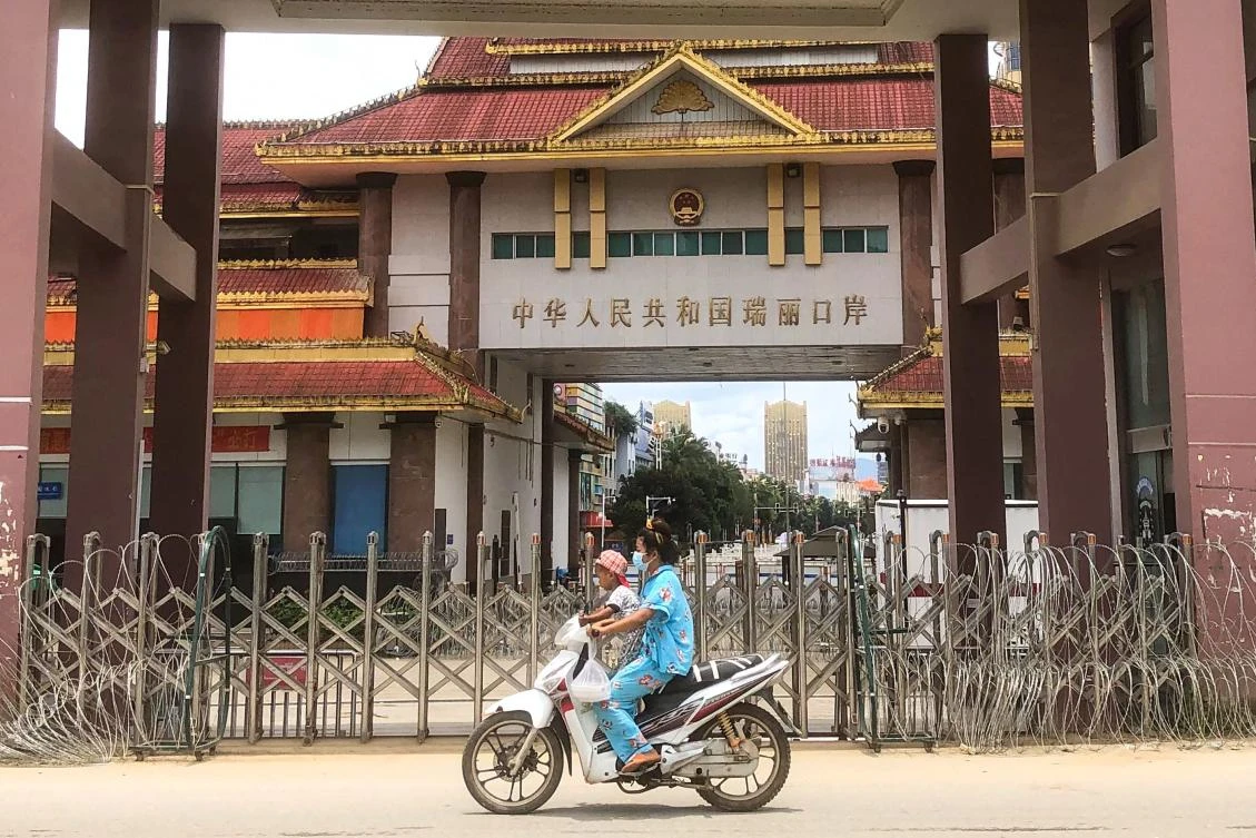 A woman rides a scooter with a child past the China-Myanmar border gate in Muse in Shan state on July 5, 2021. (AFP)