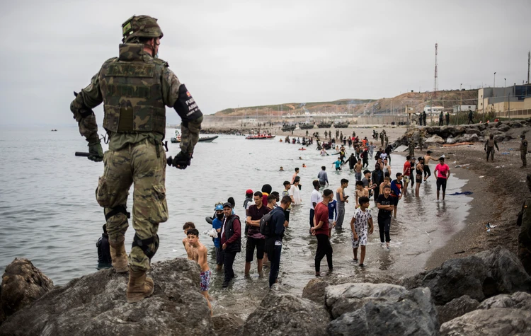 People mainly from Morocco stand on the shore as the Spanish Army cordons off a beach at the border of Morocco and Spain in the Spanish enclave of Ceuta on May 18. (AP/File Photo)