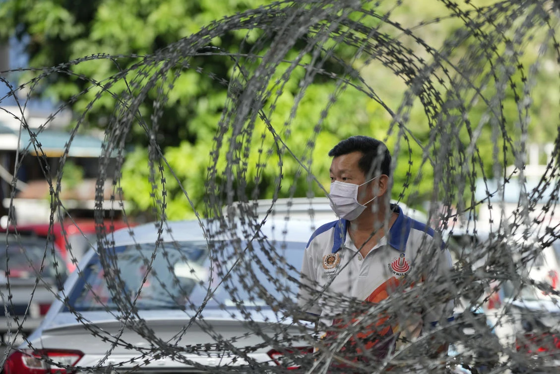 A man wearing a face mask stands next to barbwire outside a high density residential area placed under the enhanced movement control order (EMCO) due to drastic increase in the number of COVID-19 cases recorded in Bukit Jalil. (AP)