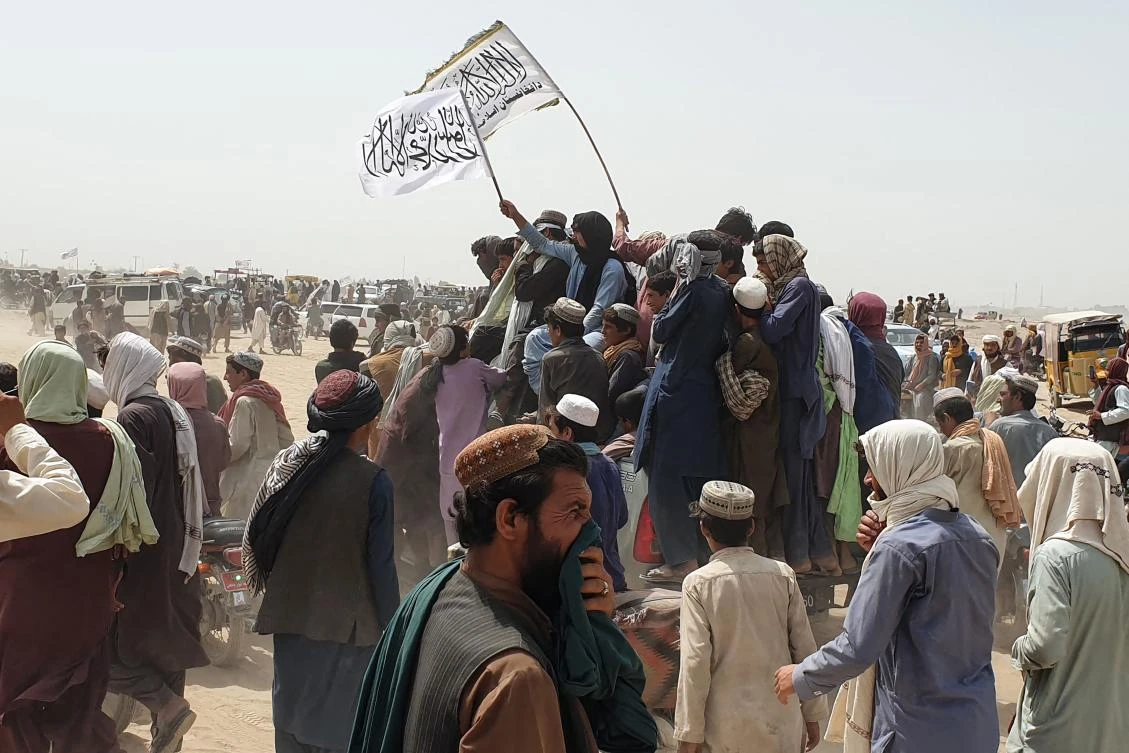 People wave Taliban flags as they drive through the Pakistani border town of Chaman on July 14, 2021, after the Taliban claimed they had captured the Afghan side of the border crossing with Pakistan. (AFP)