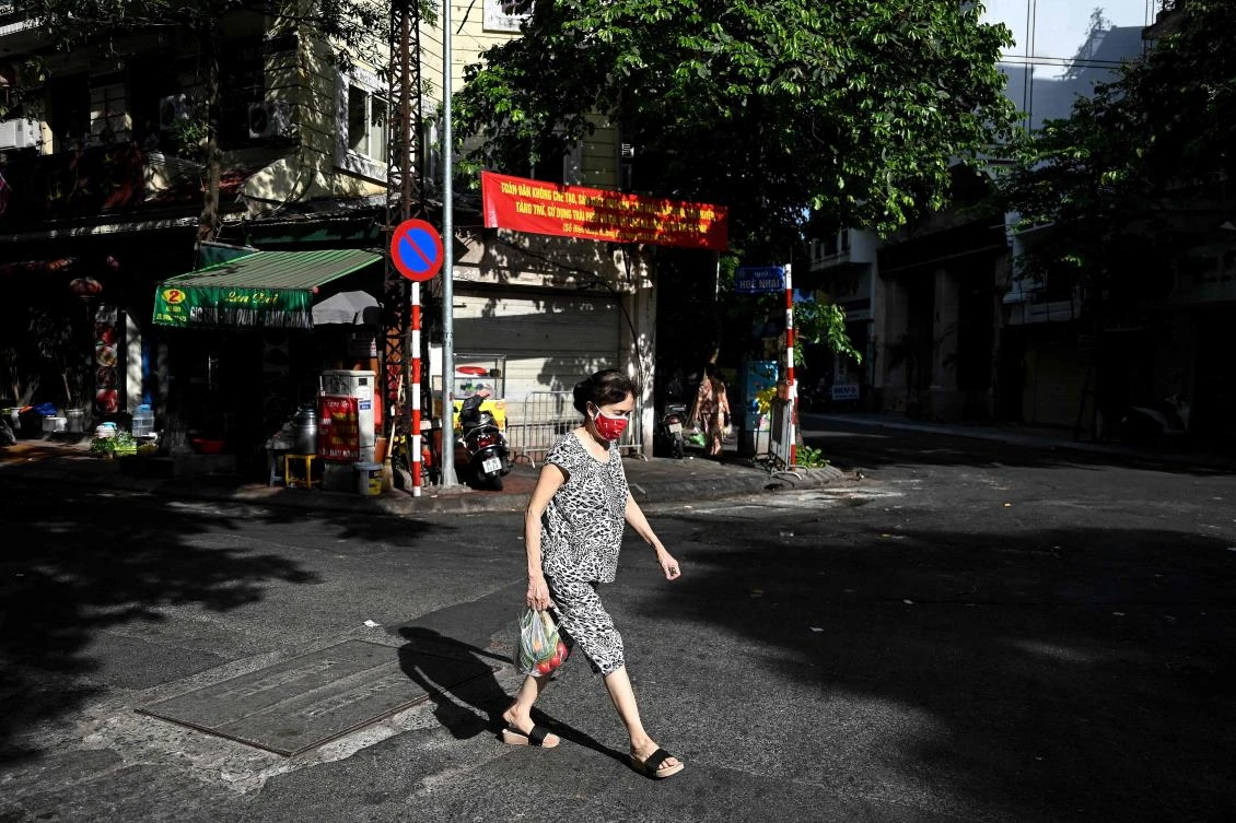 A woman wearing a face mask carries vegetables across a street in Hanoi on July 15, 2021. (AFP)