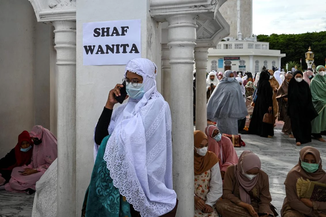 A woman speaks on her phone as Muslims arrive to attend prayers to mark the Eid al-Adha festival at the Baiturrahman Grand Mosque in Banda Aceh on July 20, 2021. (AFP)
