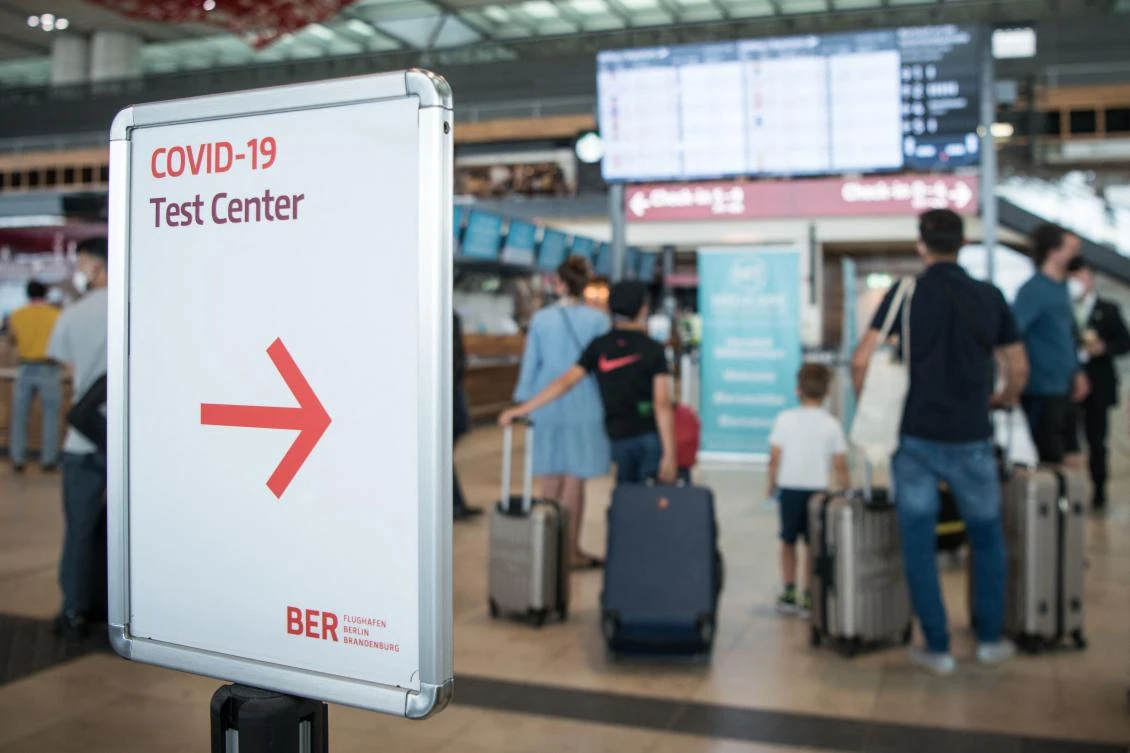 Passengers near a display board for departures next to a sign pointing to a Covid-19 test center at BER “Willy Brandt” airport near Berlin. Testing is compulsory for all travelers without proof of vaccination nor proof of recovery. (AFP)