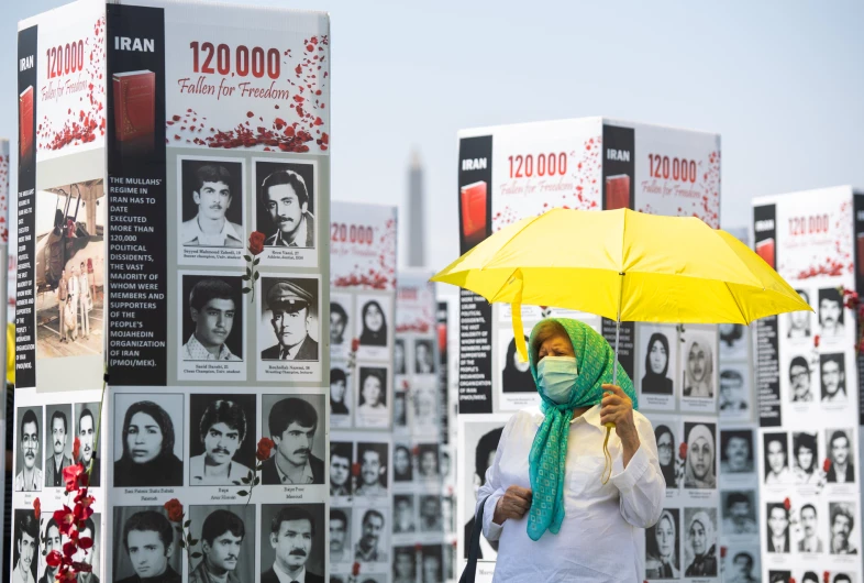 In this file photo taken on September 04, 2020 a woman with an umbrella walks past some of the thousands of photos of people killed in Iran during the 1988 massacre in Washington, DC. (AFP/ FILE)