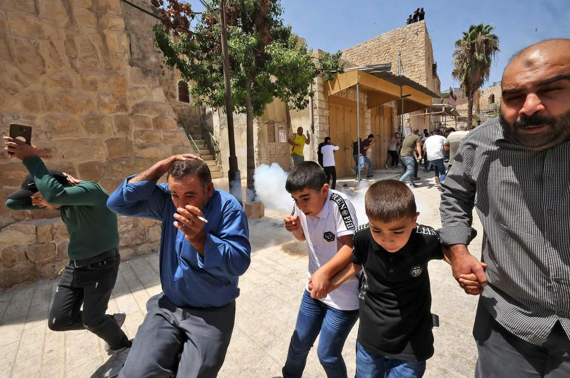 Palestinian worshipers run to avoid tear gas amid clashes with Israeli security forces at a demonstration following the Friday prayers at the Ibrahimi mosque in the occupied West Bank on August 13, 2021. (AFP)