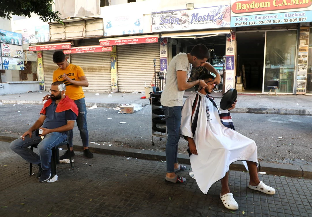 Barbers shave their customers outside their shop due to a power cut in Beirut, Lebanon, August 20, 2021. (Reuters)