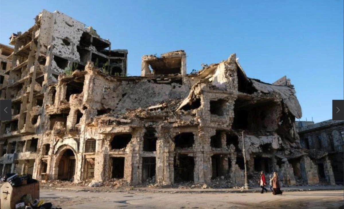 People wa;l by buildings destroyed by the war, near the old popular market know as Soukal-Jureif in Libya. (Reuterd)
