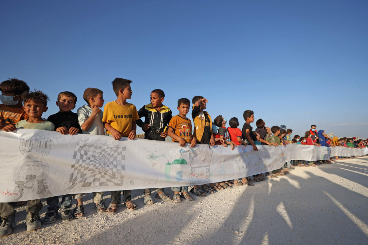 Syrian children hold a paper roll with their drawings and messages to mark the International Day of Peace at a refugee camp in Maarrat Misrin, Indlib, Syria, on Sept. 21, 2021. (Photo by Omar Haj Kadour / AFP)