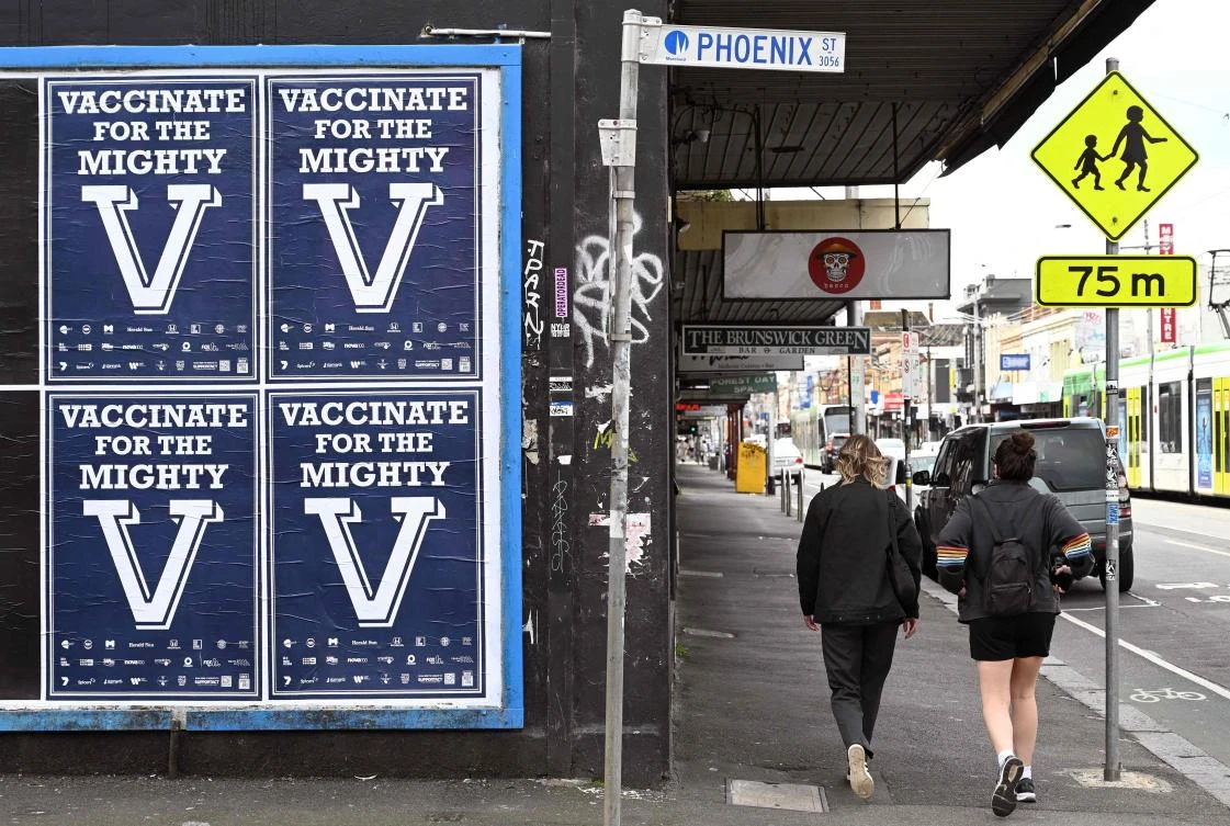 People walk past a sign encouraging people to get vaccinated in Melbourne on August 31, 2021 as the city experiences it's sixth lockdown as it battles an outbreak of the Delta variant of coronavirus. (AFP)