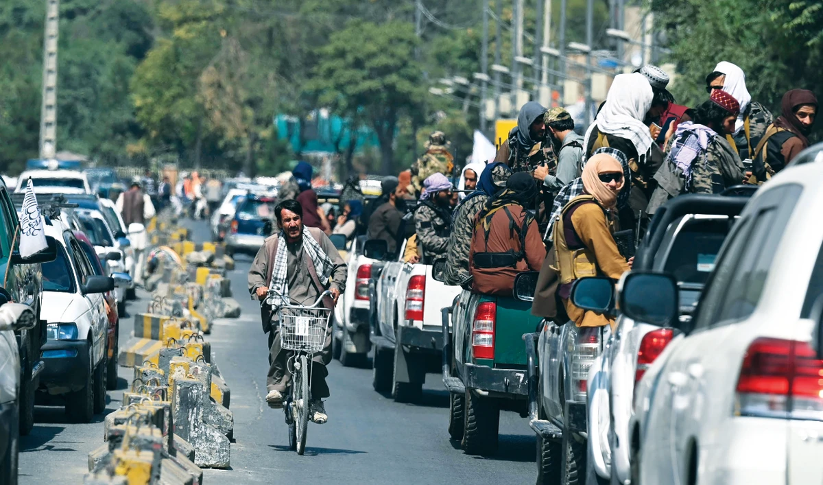 A man on his bicycle rides past a convoy of Taliban fighters patrolling along a street in Kabul on Thursday. The Taliban are preparing to unveil their new government. (AFP)