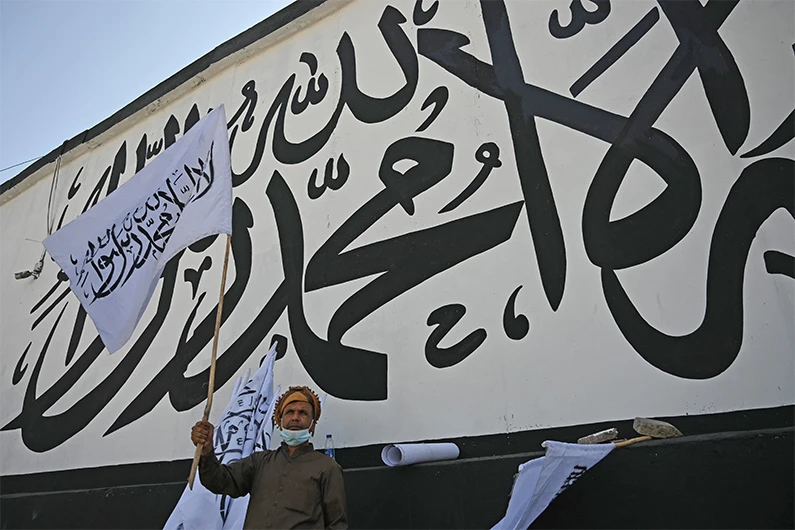An Afghan street vendor carries a Taliban beside outer concrete wall of US embassy with mural of Taliban flag in Kabul on September 8, 2021. (AFP)