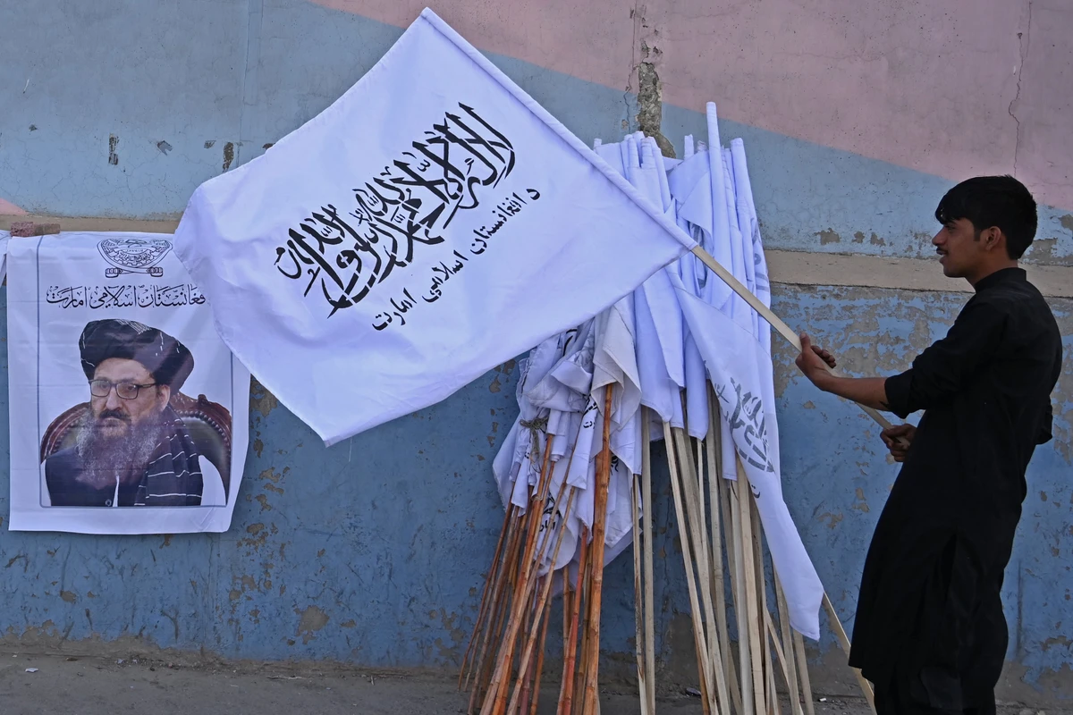A vendor holds a Taliban flag next to a poster of Taliban leader Abdul Ghani Baradar as he waits for customers along a street in Kabul on August 27, 2021. (AFP)