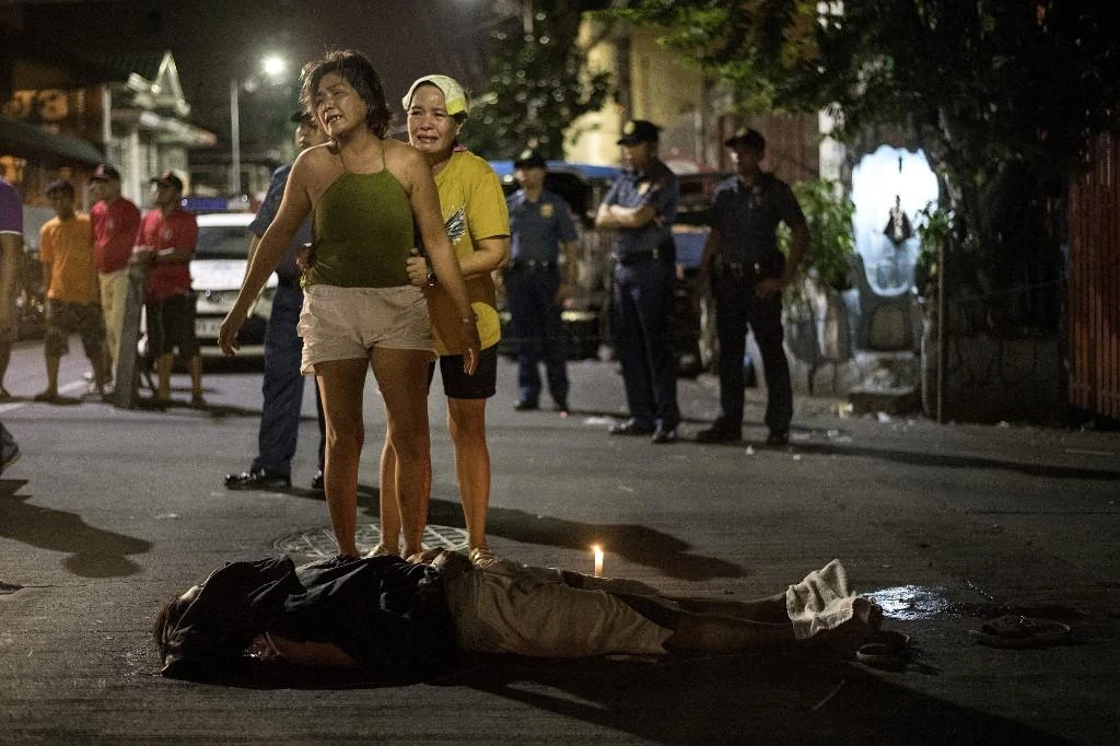 A resident grieves beside the body of her son, an alleged drug user killed by unidentified assailants, in Manila on Oct. 3, 2017 while police look on. (AFP)