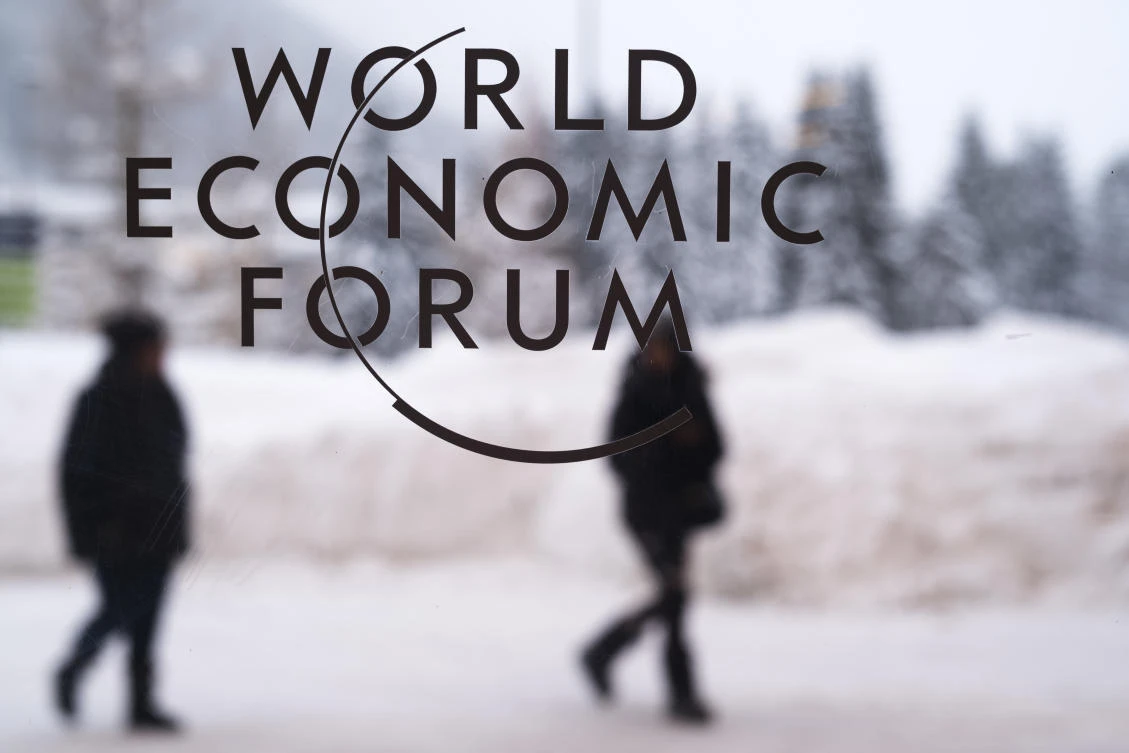 Two people walk behind the logo of the World Economic Forum at the meeting's conference center in Davos, Switzerland. (AP Photo)