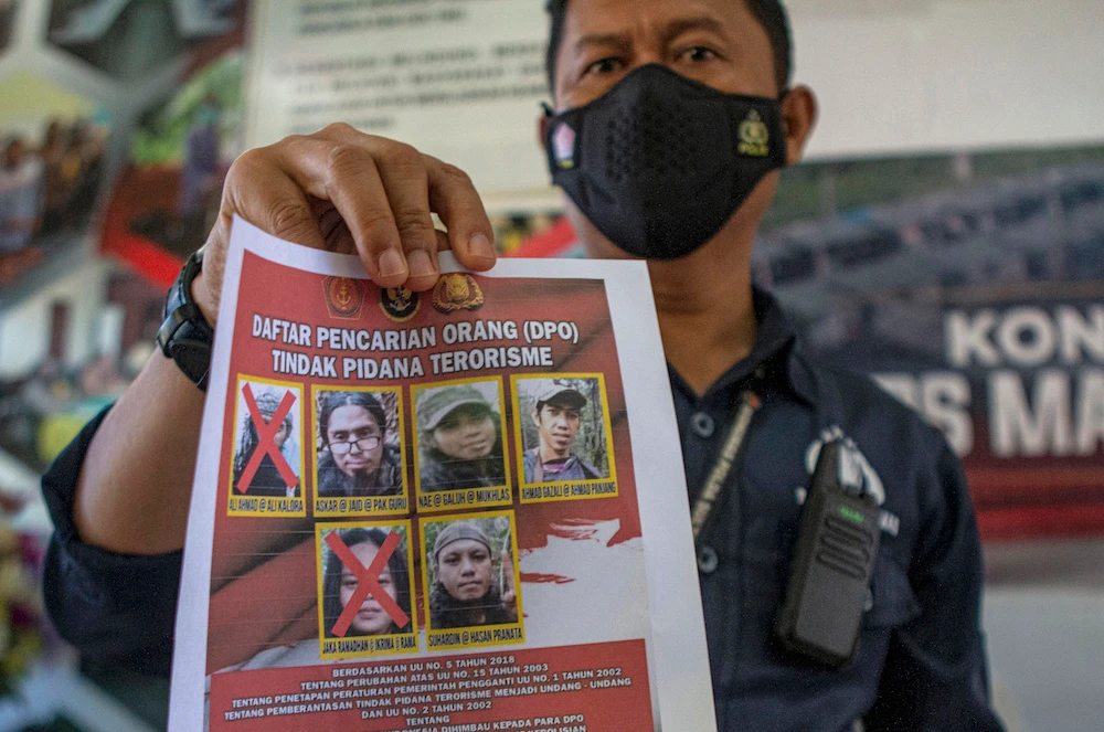 A police officer shows a wanted poster displaying the photos of two militants Ali Kalora, top left, and Jaka Ramadan, bottom left, who were killed during shootout with security forces. (AP)