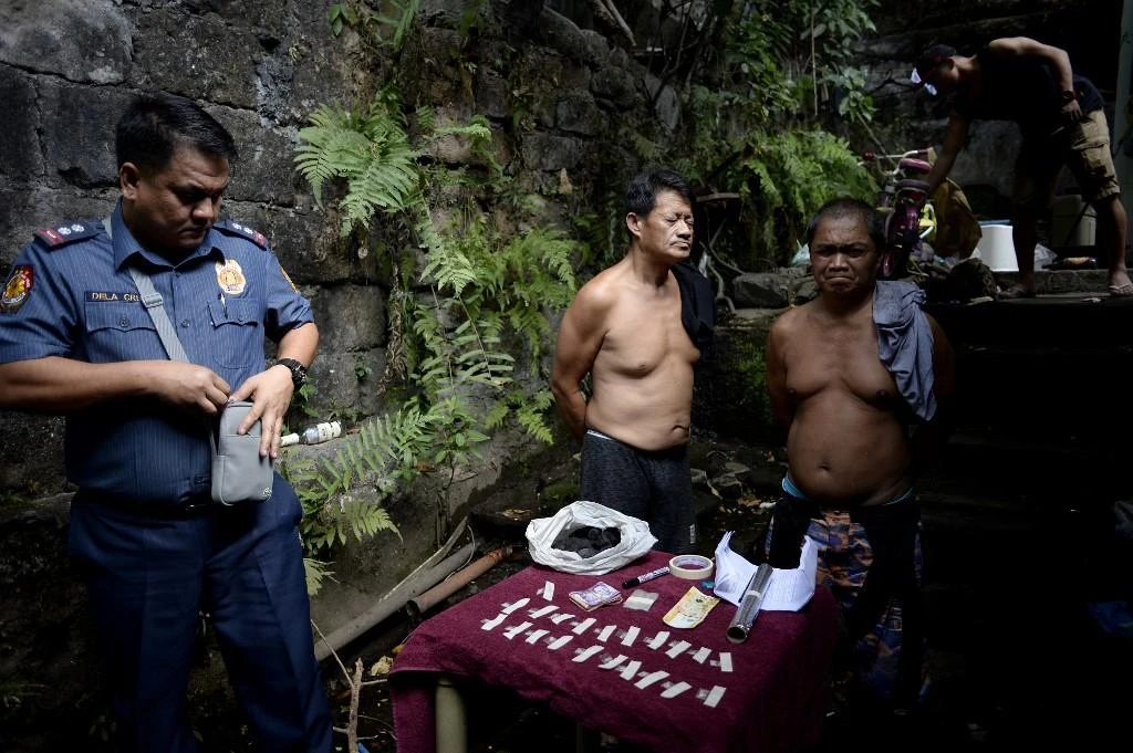 Two alleged drug dealers stand next to drug paraphernalia confiscated during a police operation conducted in Manila on March 15, 2018. (AFP)