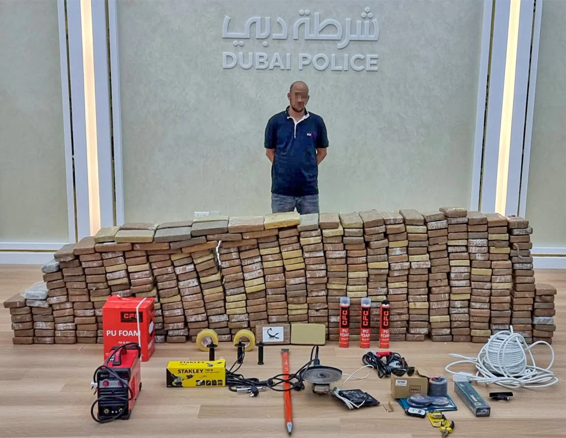 This handout picture provided by the Dubai Police Force on October 10, 2021, shows a suspect arrested by the Dubai Police Force, standing behind seized drugs and tools in the Gulf emirate. (AFP)