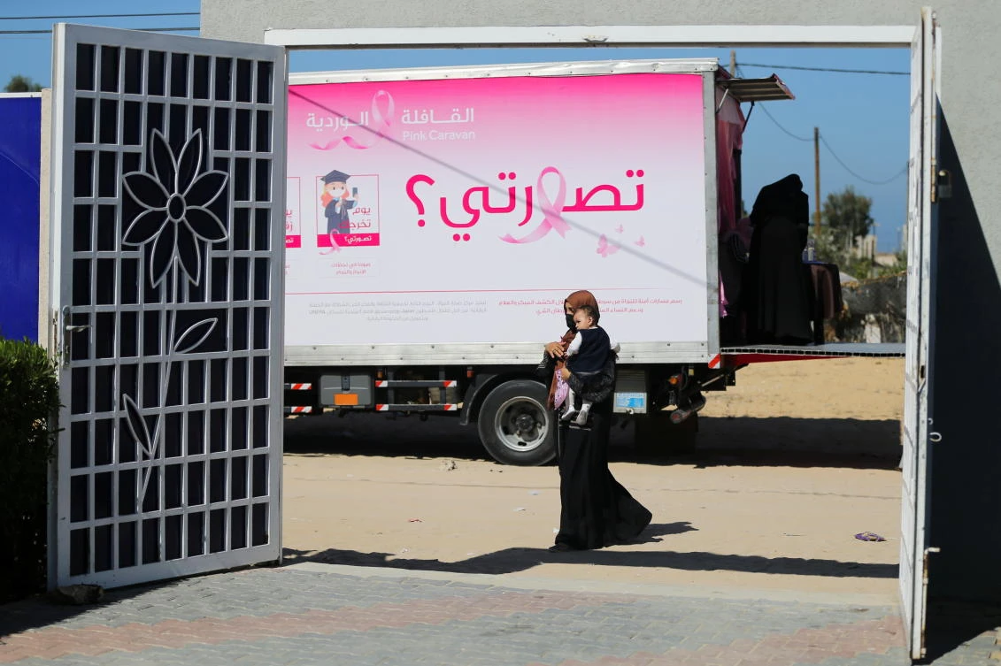 A Palestinian woman with a child walks past a mobile breast cancer check up clinic set up in a truck. Picture taken October 7, 2021. (Reuters)