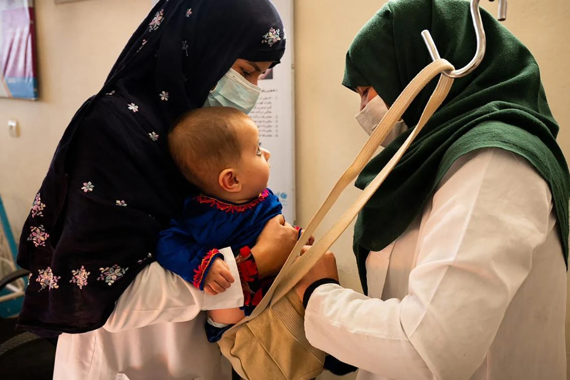 This picture taken on October 6, 2021 shows a midwife (L) and a nutrition counselor weighing a baby at the Tangi Saidan clinic run by the Swedish Committee for Afghanistan, in Daymirdad district of Wardak province. (AFP)