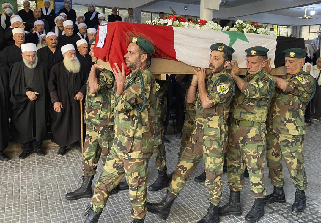 Volunteers from the Baath battalions carry the Syrian flag-wrapped coffin of former Syrian Druze lawmaker Midhat Saleh during his funeral procession in Jaramana, southeast of Damascus on Monday. (AP)