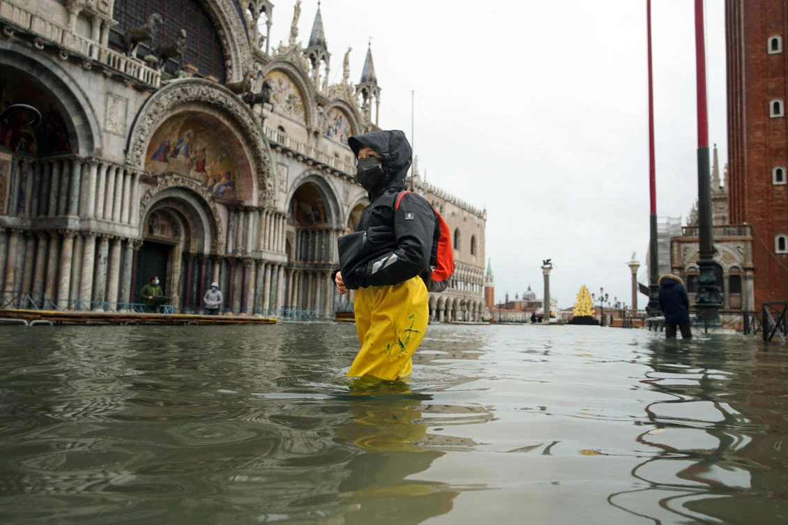In this Tuesday, Dec. 8, 2020 file photo, people wade their way through water in flooded St. Mark's Square following a high tide, in Venice, Italy. (File/AP)