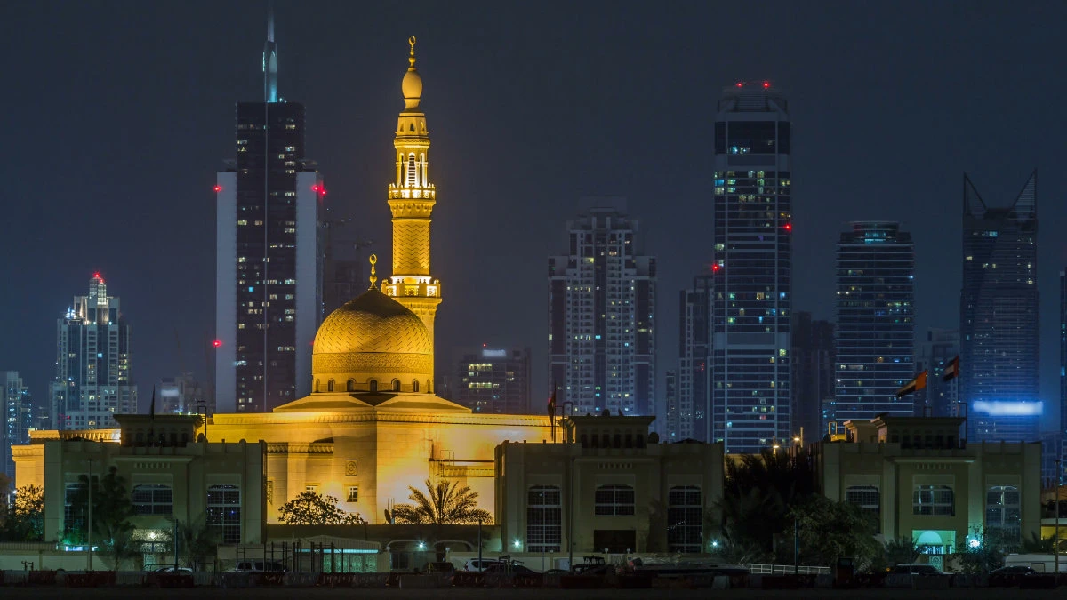 Modern Dubai city skyline timelapse with Rashid Al Hadeeth Mosque at night with illuminated skyscrapers over water surface. (Shutterstock image)