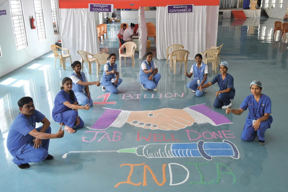 Medical staff pose next to a Rangoli design on the floor of the Ramaiah Hospital in Bangalore, as they celebrate India administering its billionth COVID-19 vaccine dose. (AFP)