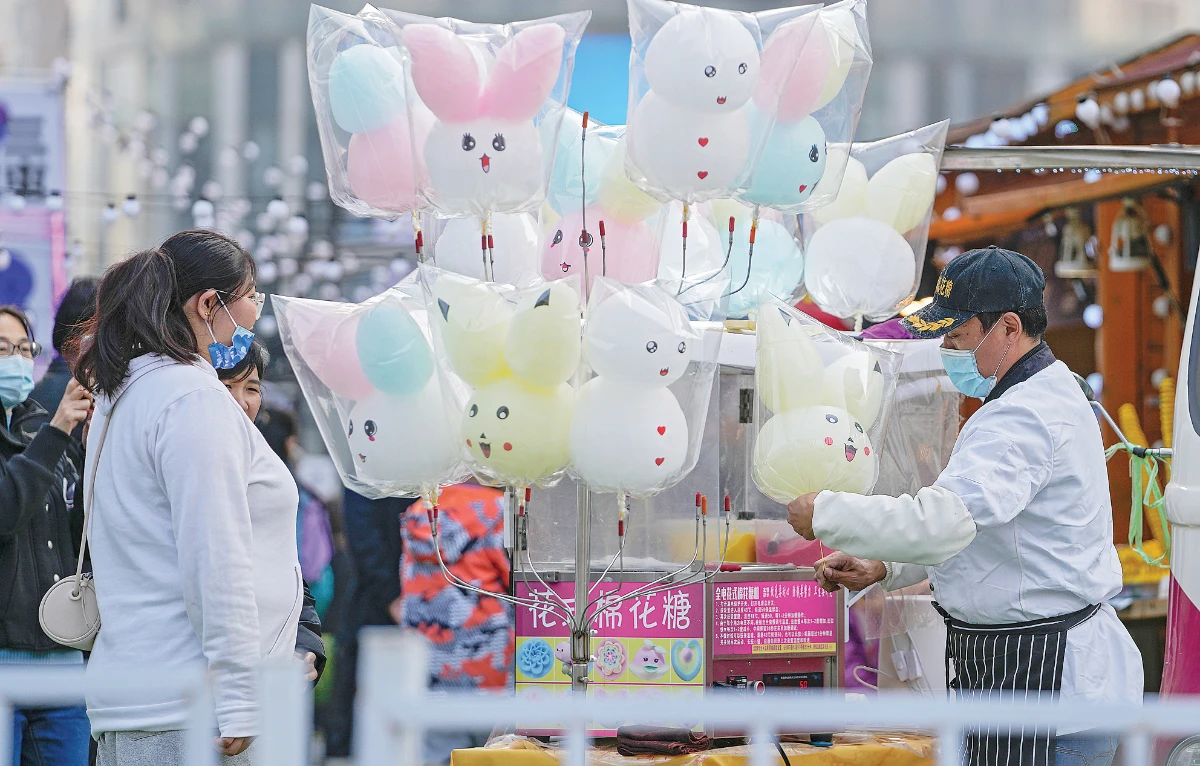 A vendor makes cotton candy for his customers during a carnival at a shopping mall in Beijing on Sunday. China has given complete doses of vaccines to about 76 percent of its population as of Oct. 23. (AP)