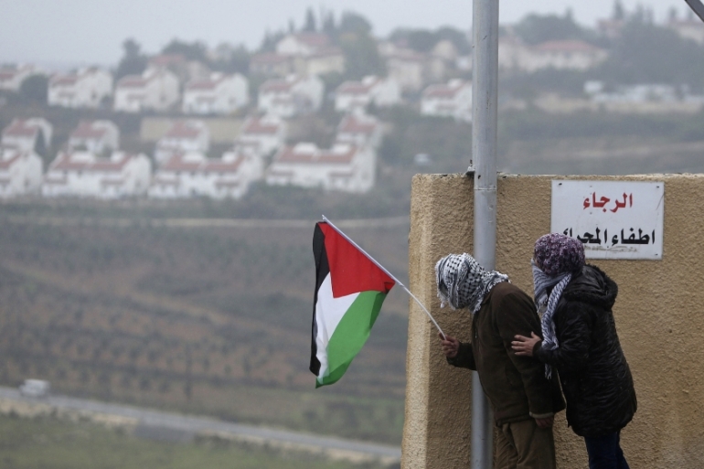 Protesters fly the Palestinian flag against the backdrop of the Israeli settlement of Halamish. (Reuters)