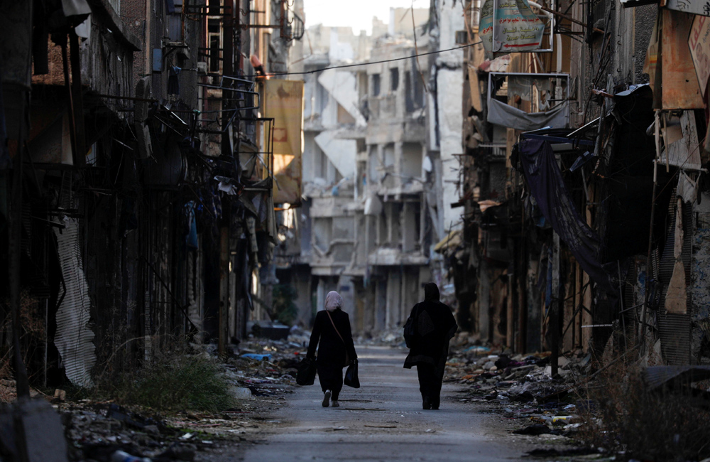 Women walk past damaged buildings in the Yarmouk Palestinian refugee camp on the southern outskirts of Damascus, Syria, Dec. 1, 2020. (Reuters)