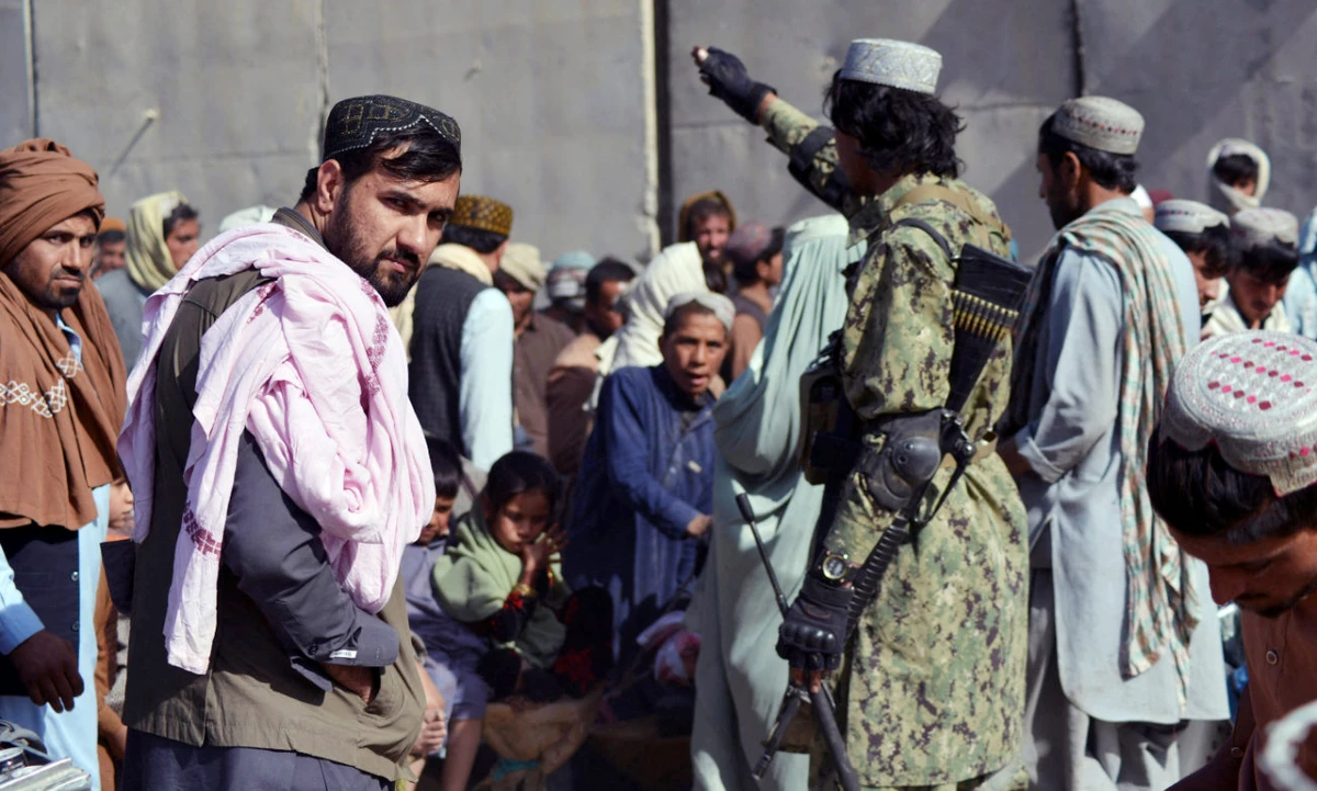 A Taliban fighter (R) gestures to people waiting to cross into Pakistan at the Afghanistan-Pakistan border crossing point in Spin Boldak on November 3, 2021, after authorities reopened the border following nearly a month-long closure. (AFP)