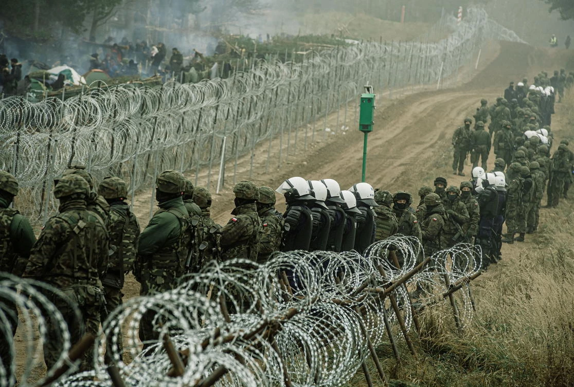 Polish soldiers and police watch migrants at the Poland/Belarus border near Kuznica, Poland, in this photograph released by the Territorial Defense Forces on Friday. (Reuters)